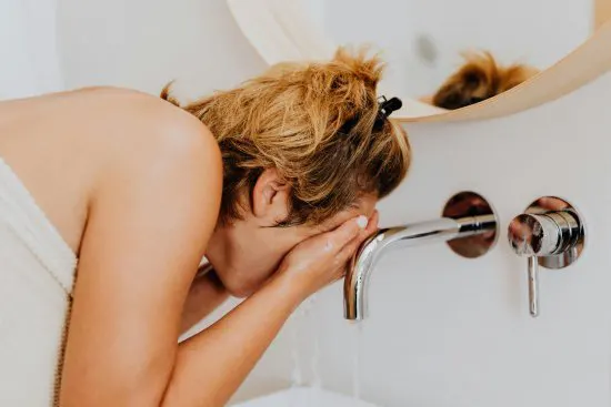 Mujer lavando su rostro con agua dura del grifo.